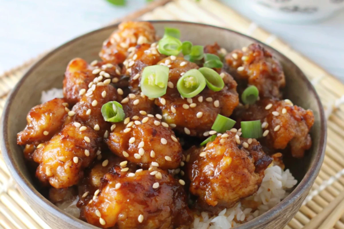 Honey Garlic Chicken garnished with sesame seeds and green onions on a white plate.